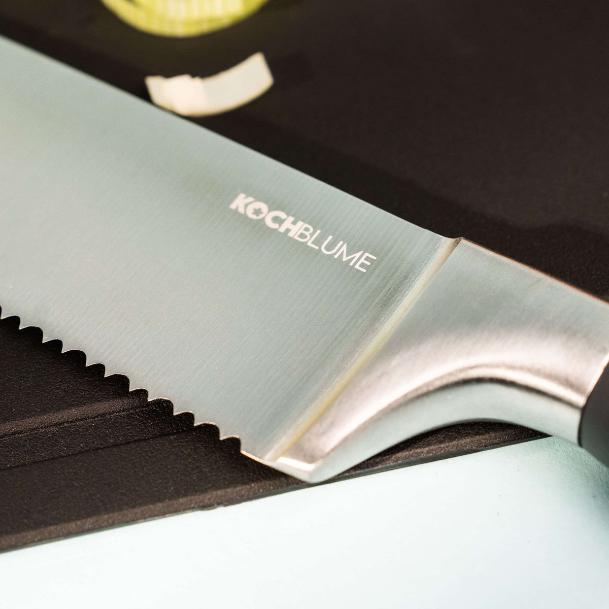 Gros plan sur un couteau de cuisine dentelé « Chefmesser » de la marque Kochblume GmbH, posé sur une planche à découper noire, avec une gousse d'ail à côté. Veuillez fournir une description détaillée du couteau de cuisine « Chefmesser » de Kochblume GmbH afin de permettre une extraction précise des mots-clés pour le référencement naturel (SEO), car les informations actuelles sont insuffisantes à cette fin.