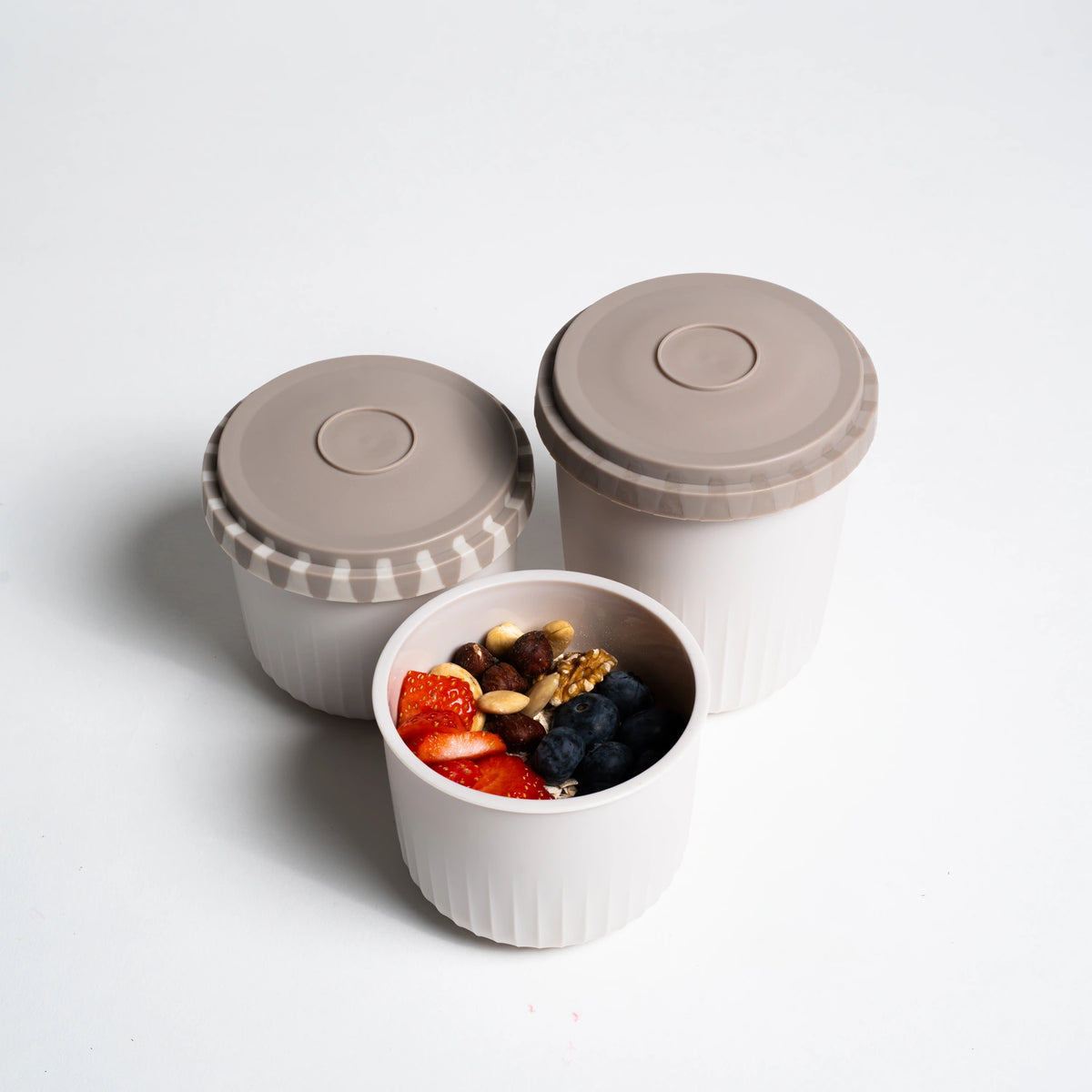 Drei weiße Snackboxen der Firma Kochblume GmbH mit taupefarbenen Deckeln; eine ist geöffnet und gibt den Blick auf Beeren und Nüsse im Inneren frei – die perfekte, auslaufsichere Snackbox für unterwegs.