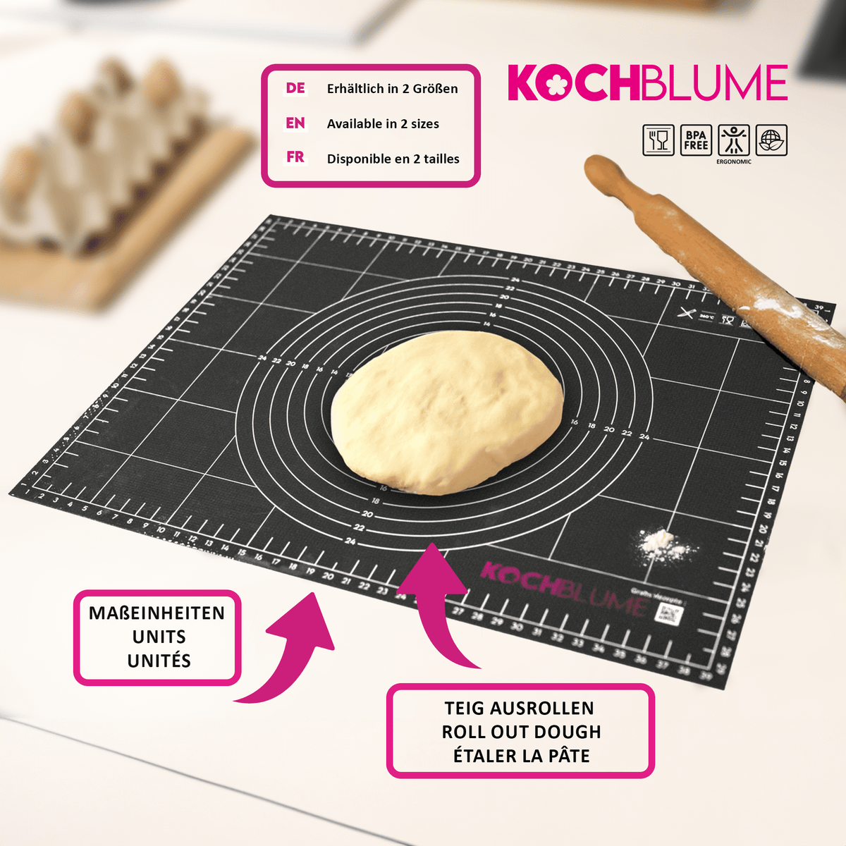 A Gewebematte by Kochblume GmbH—a black silicone baking mat featuring measurement markings, shown with dough in the center and a rolling pin.
