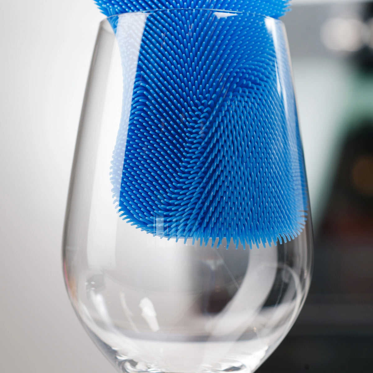 Der „Scrubby“ der Kochblume GmbH, ein blauer Silikon-Reiniger, reinigt mühelos das Innere eines klaren Weinglases und sorgt dafür, dass jede Oberfläche glänzt, ohne Kratzer zu hinterlassen.