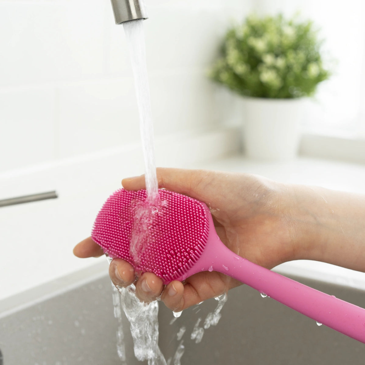 Wenn Sie die „Universalbürste“ von Kochblume GmbH – eine rosa Silikon-Scheuerbürste – unter fließendem Wasser in Ihrem Spülbecken abspülen, sorgen Sie für eine gründliche Reinigung und tragen dazu bei, die Lebensdauer Ihrer Küchenutensilien zu verlängern.