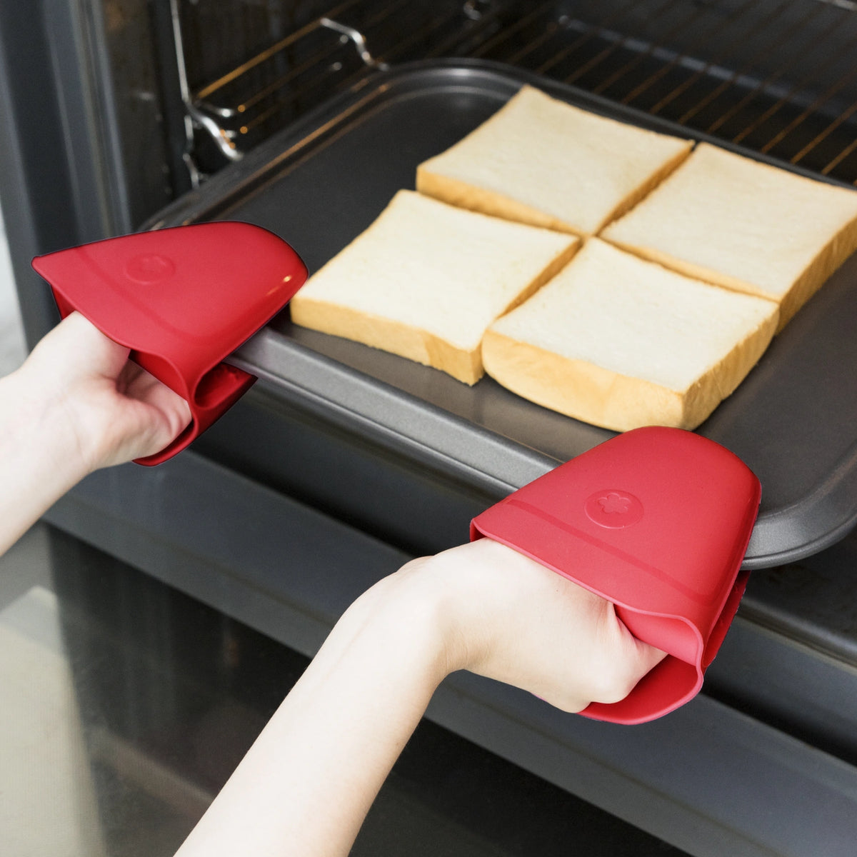 Mit den Thermo-Fingerschutz-Backhandschuhen der Kochblume GmbH werden die Hände vorsichtig aus dem Ofen gezogen, auf denen ein Blech mit vier goldbraunen Brotscheiben liegt – perfekt für Ihren nächsten leckeren Snack.