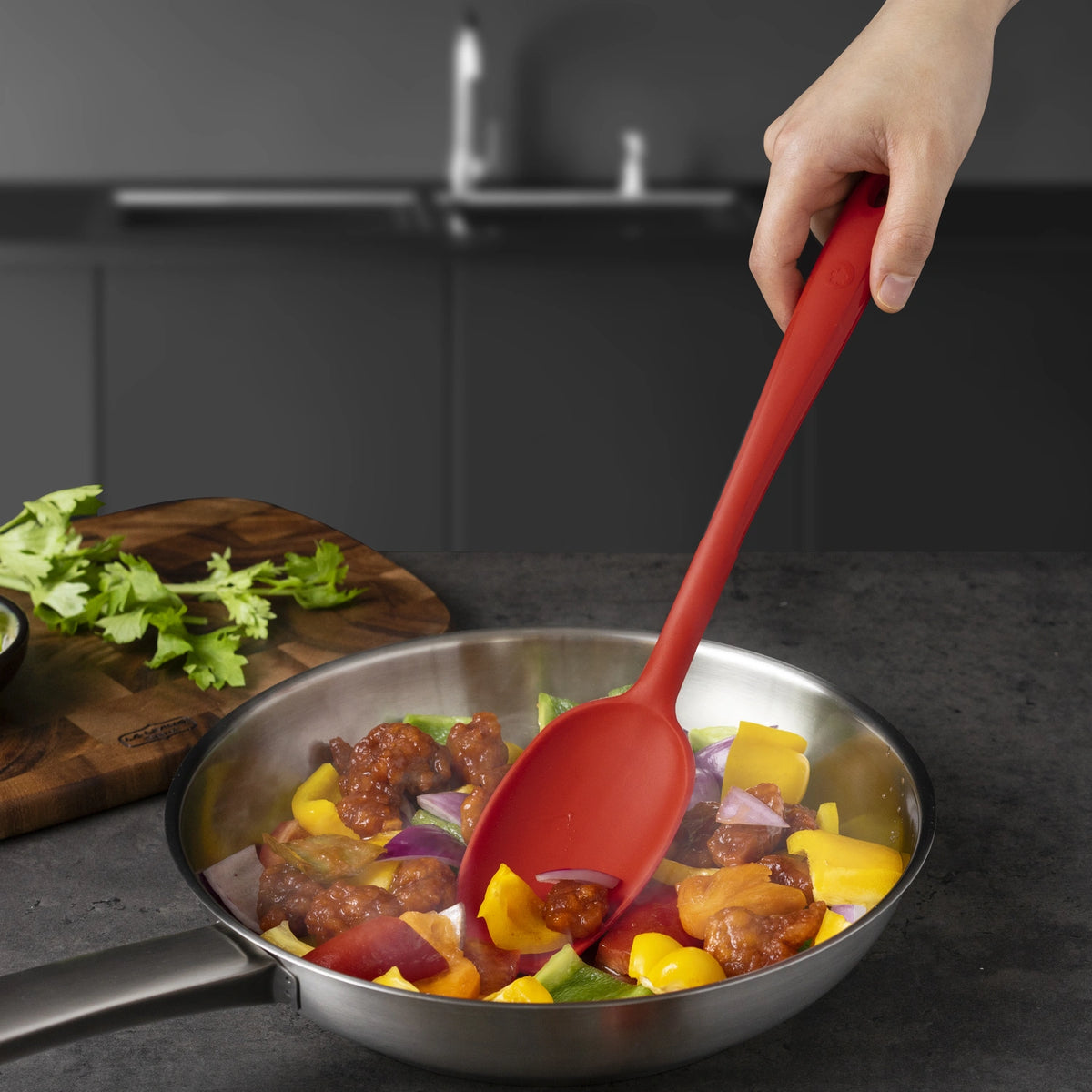 Eine Hand rührt auf einer Küchenarbeitsplatte bunte Gemüsestücke und Fleisch in einer Pfanne mit dem Soßenlöffel der Kochblume GmbH um – einem hochwertigen Soßenlöffel, der für präzises Umrühren und Servieren entwickelt wurde. Wichtige SEO-Schlüsselwörter: Soßenlöffel, Kochblume GmbH, Soßenlöffel.