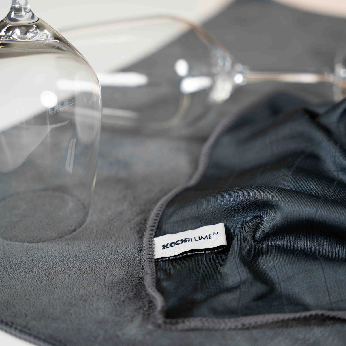 Two upside down wine glasses rest elegantly on a grey cloth labeled “Poliertuch” by Kochblume GmbH, though the image lacks additional meaningful product details.