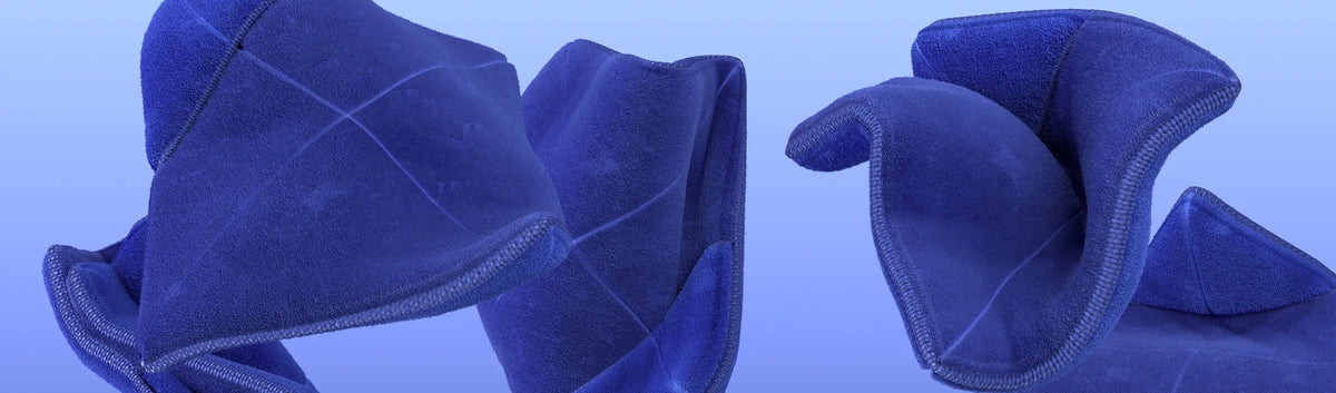 Drei abstrakte, geschwungene Formen aus blauem, wildlederähnlichem Stoff vor einem hellblauen Hintergrund mit Farbverlauf.