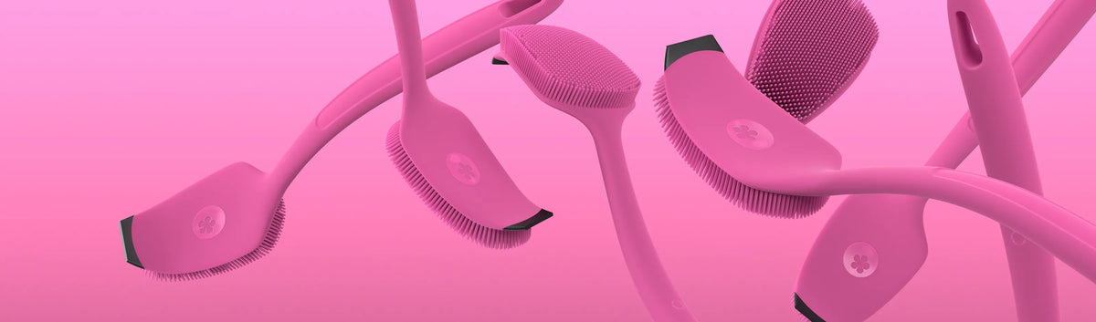 Mehrere rosa Silikonpinsel mit langen Stielen schweben vor einem rosa Hintergrund mit Farbverlauf.