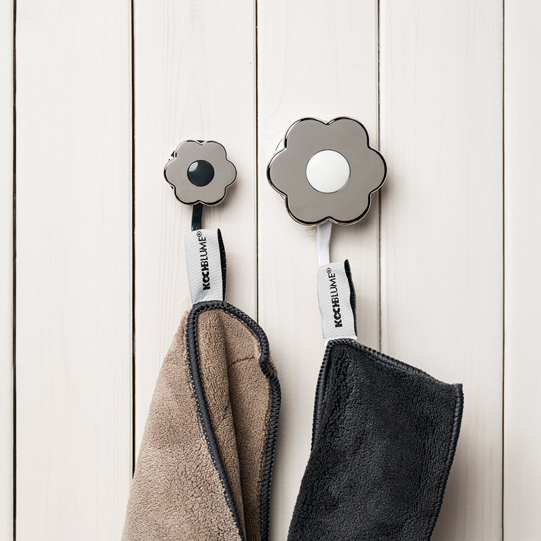 An dem „Blumenhaken-Set“ der Kochblume GmbH hängen zwei Handtücher. Die blumenförmigen Haken sind an einer weißen Holzwand befestigt und sorgen für eine charmante und aufgeräumte Präsentation.