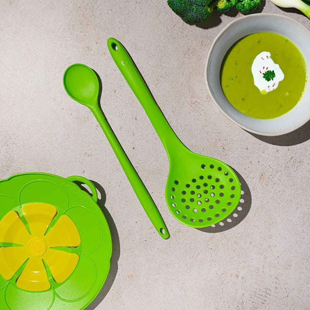 Zwei grüne Küchenutensilien neben einer Schüssel mit grüner Suppe und einem grün-gelben Silikon-Dampfkorb.