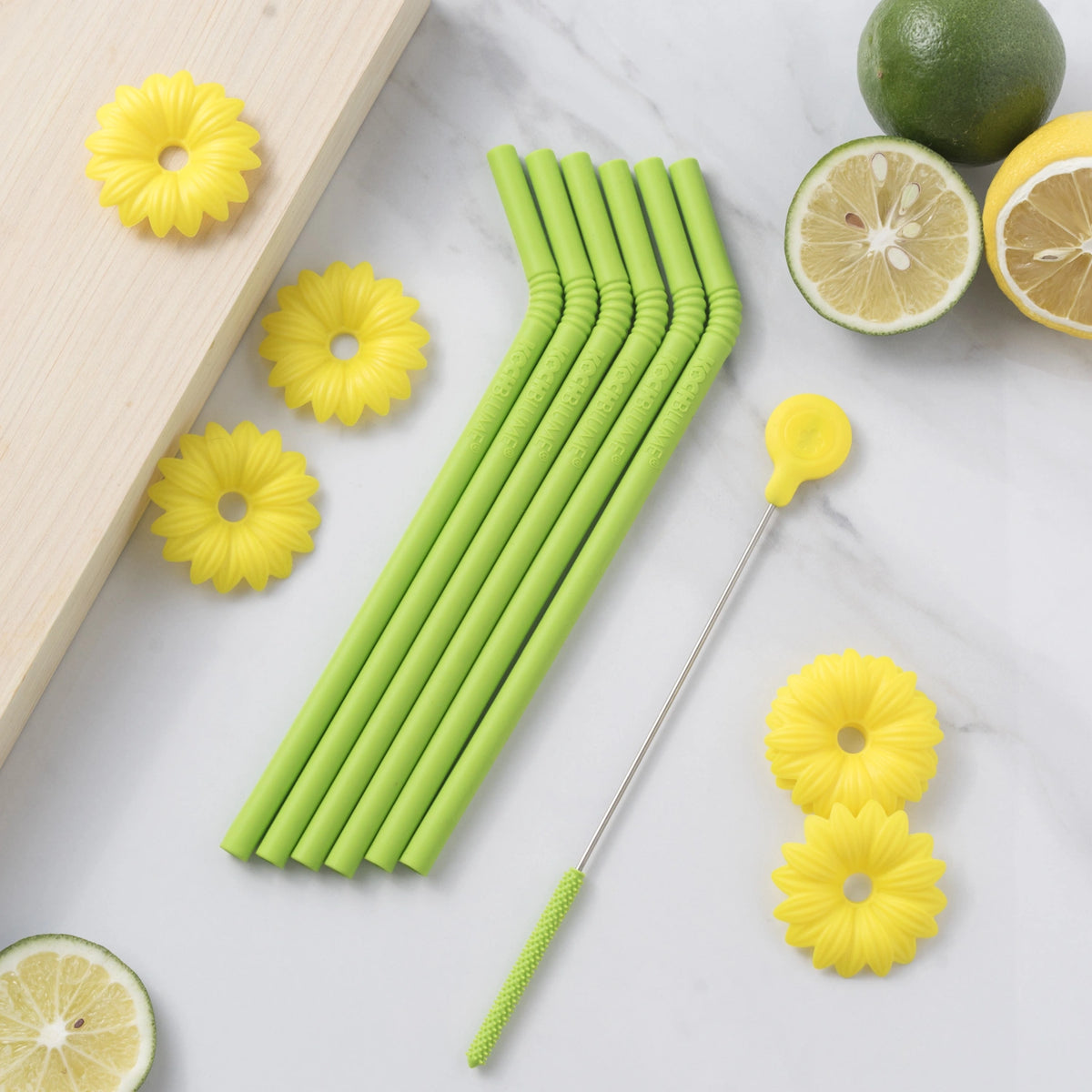 Die Trinkhalme von Kochblume GmbH – grüne, wiederverwendbare Strohhalme mit gelben, blumenförmigen Aufsätzen und einer praktischen Reinigungsbürste – sind elegant auf einer Marmorfläche inmitten von leuchtend bunten Zitrusfrüchten arrangiert und sind damit die perfekte umweltfreundliche Ergänzung zu Ihren Lieblingsgetränken.