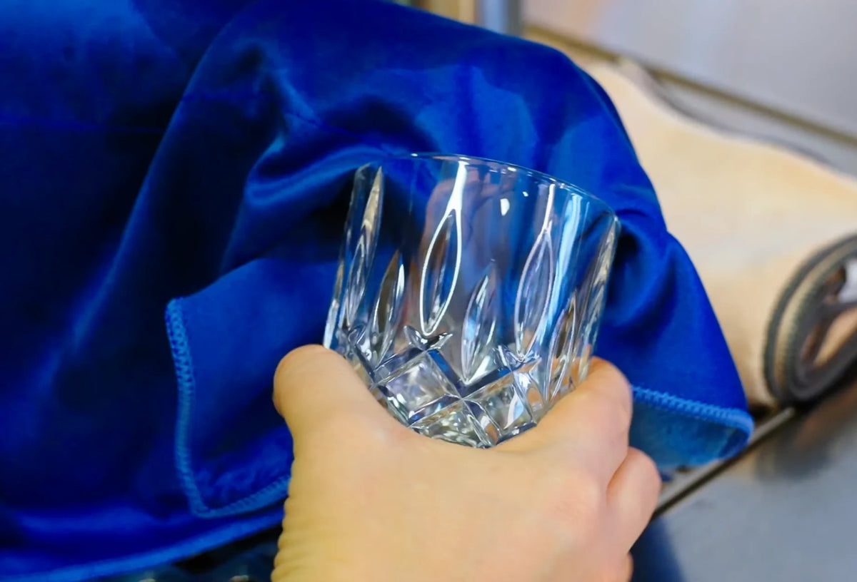 Eine Hand poliert ein klares Glas mit einem hellblauen Tuch.
