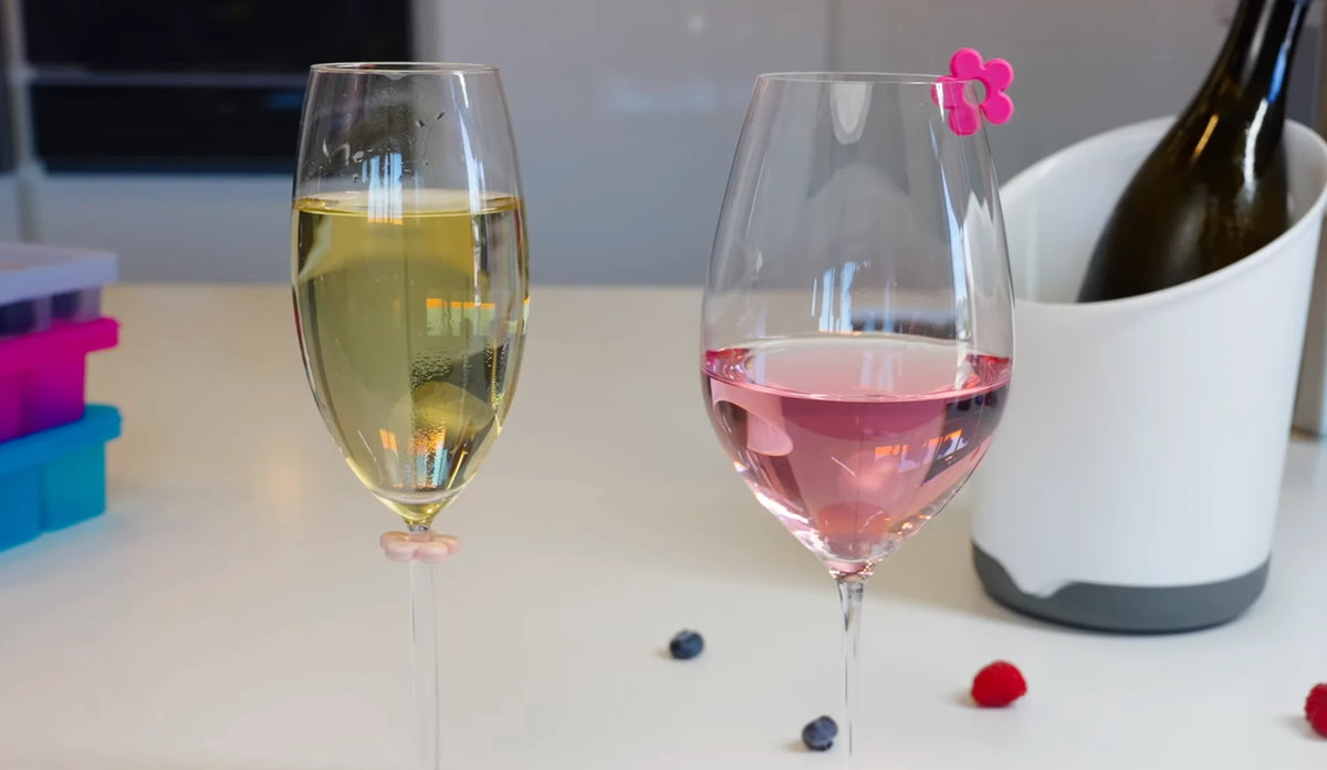 Zwei Gläser, eines mit Champagner und eines mit Rosé, auf einem Tisch mit Beeren und einer Weinflasche in einer Kühlbox.