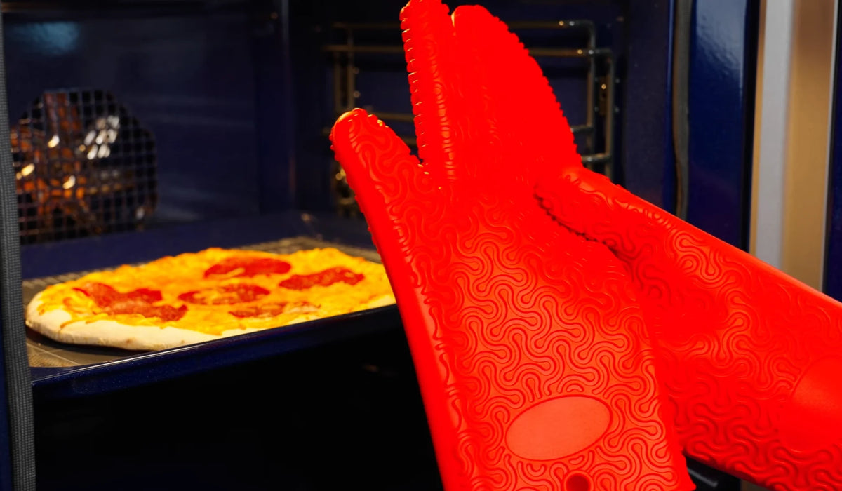 Hände in leuchtend roten Ofenhandschuhen, die eine Peperoni-Pizza aus dem Ofen nehmen.