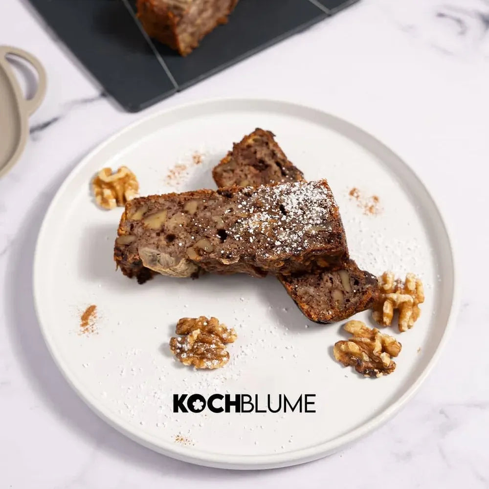 Zwei Scheiben Felix-Nussbrot der Firma Kochblume GmbH, garniert mit Walnüssen und Puderzucker, serviert auf einem weißen Teller mit der Aufschrift „KOCHBLUME“.