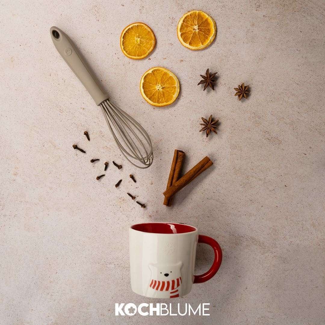 Eine Tasse, ein Schneebesen, getrocknete Orangenscheiben, Gewürze und das Kochblume-Logo, arrangiert auf einem hellen Untergrund.