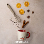 Eine Tasse, ein Schneebesen, getrocknete Orangenscheiben, Gewürze und das Kochblume-Logo, arrangiert auf einem hellen Untergrund.