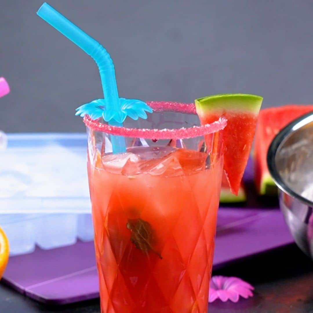 Ein Wassermelonengetränk mit Eis, einem blauen Strohhalm und einer Wassermelonenscheibe als Garnitur in einem Glas mit rosa Zuckerrand.