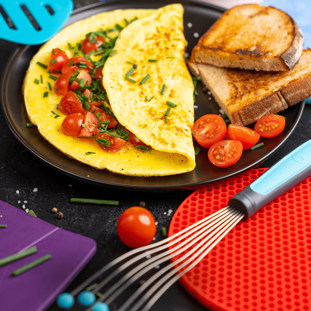 Omelett mit Kirschtomaten und Schnittlauch, serviert mit Toast und Besteck auf einem schwarzen Teller.