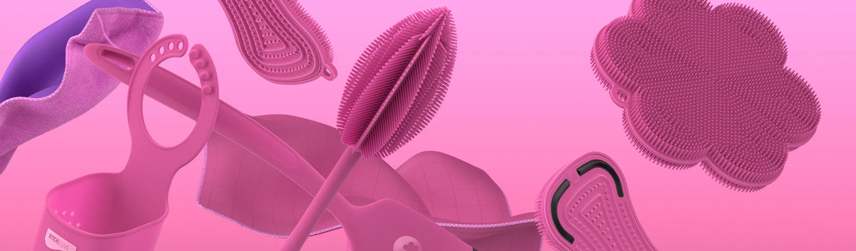 Verschiedene rosa Reinigungsutensilien aus Silikon und Tücher, die auf einem rosa Hintergrund mit Farbverlauf schweben.