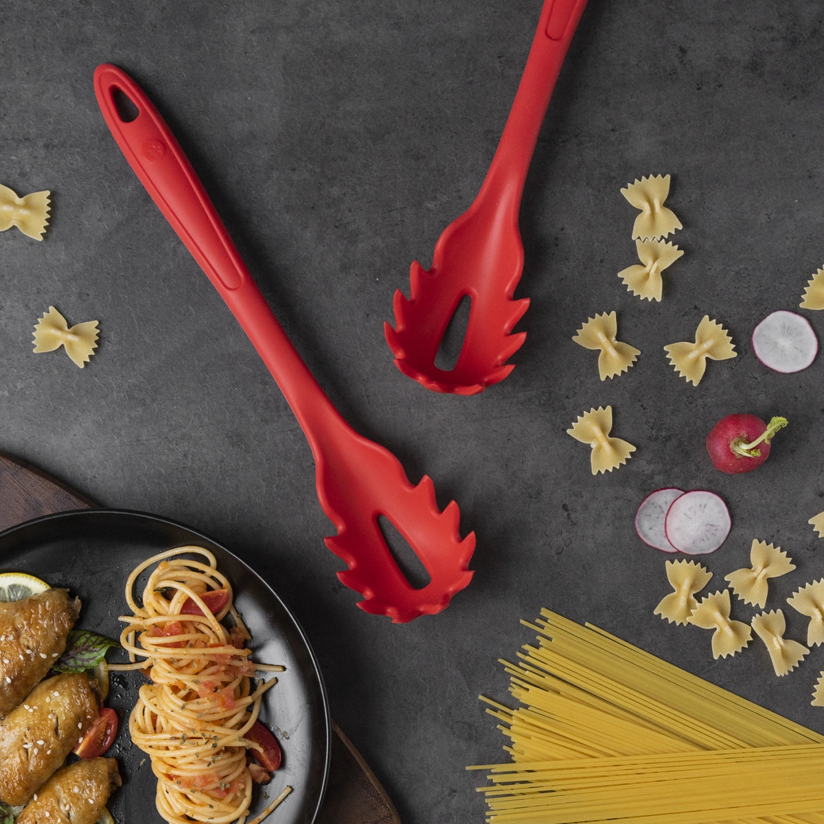 Zwei leuchtend rote „Pastalöffel“-Nudelheber der Firma Kochblume GmbH sind neben ungekochten Spaghetti, Farfalle, frischen Radieschenscheiben und einem Teller mit fertig zubereiteten Nudeln angeordnet. Die aktuelle Produktbeschreibung enthält jedoch lediglich CSS-Code und keine konkreten Angaben zu den „Pastalöffeln“. Bitte geben Sie eine vollständigere Produktbeschreibung an, damit relevante SEO-Schlüsselwörter extrahiert werden können.