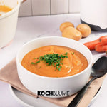Eine Schüssel cremige Orangen-Felix-Suppe von Kochblume GmbH, garniert mit gehackten Kräutern und serviert mit Kartoffeln und Möhren.