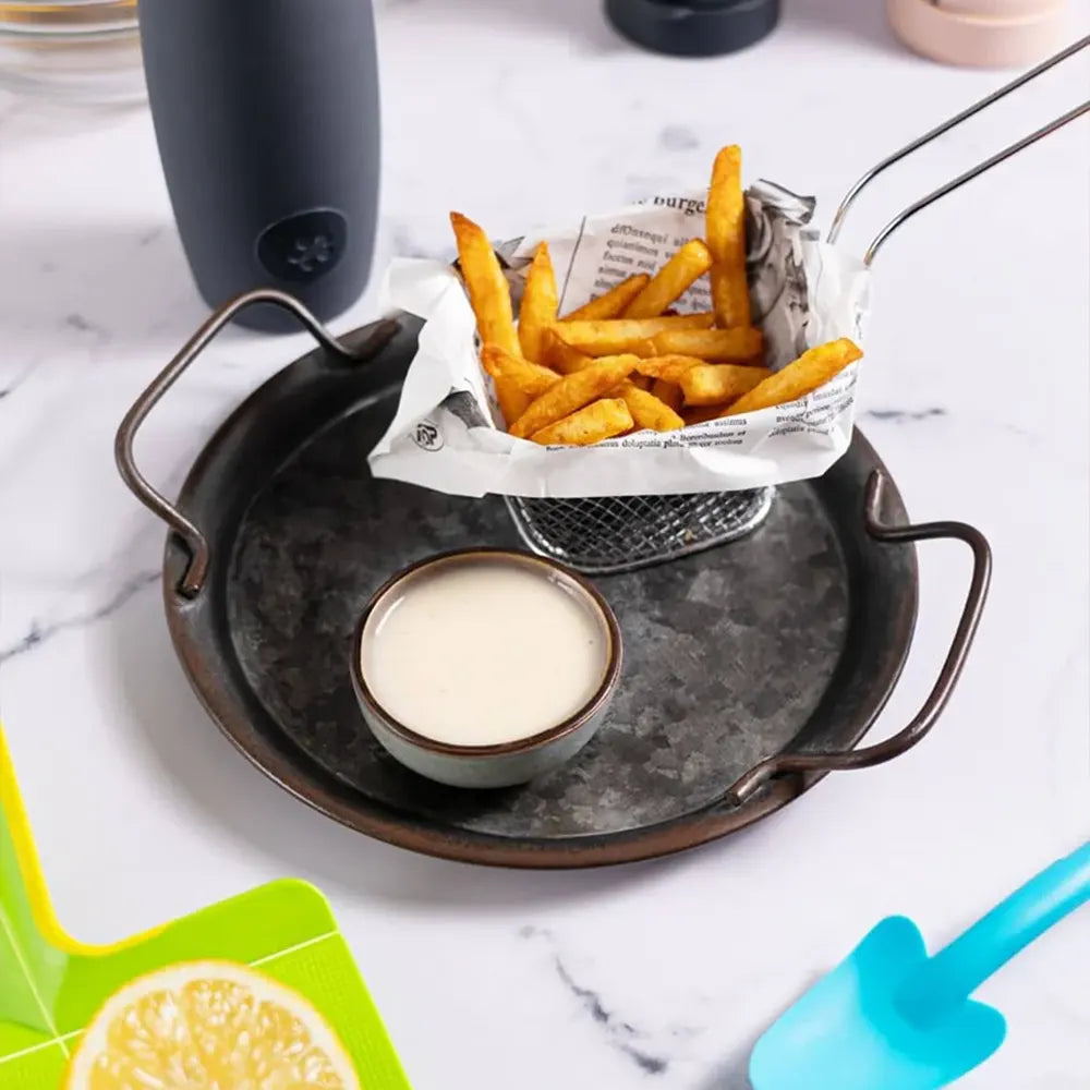 Pommes frites in einem Metallkörbchen mit einer kleinen Schale mit Dip auf einem runden Tablett, das auf einer Marmorplatte steht.