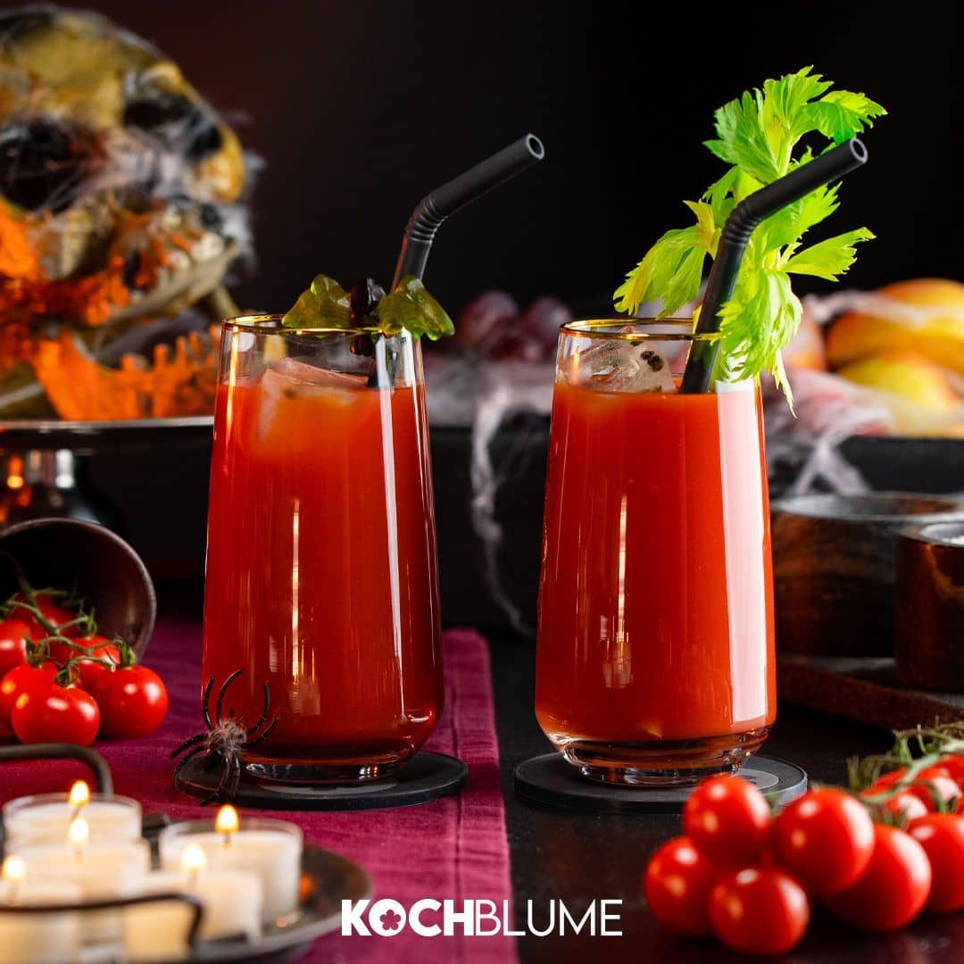 Zwei Bloody-Mary-Cocktails mit Strohhalmen, garniert mit Stangensellerie und Oliven, umgeben von Tomaten und Kerzen.